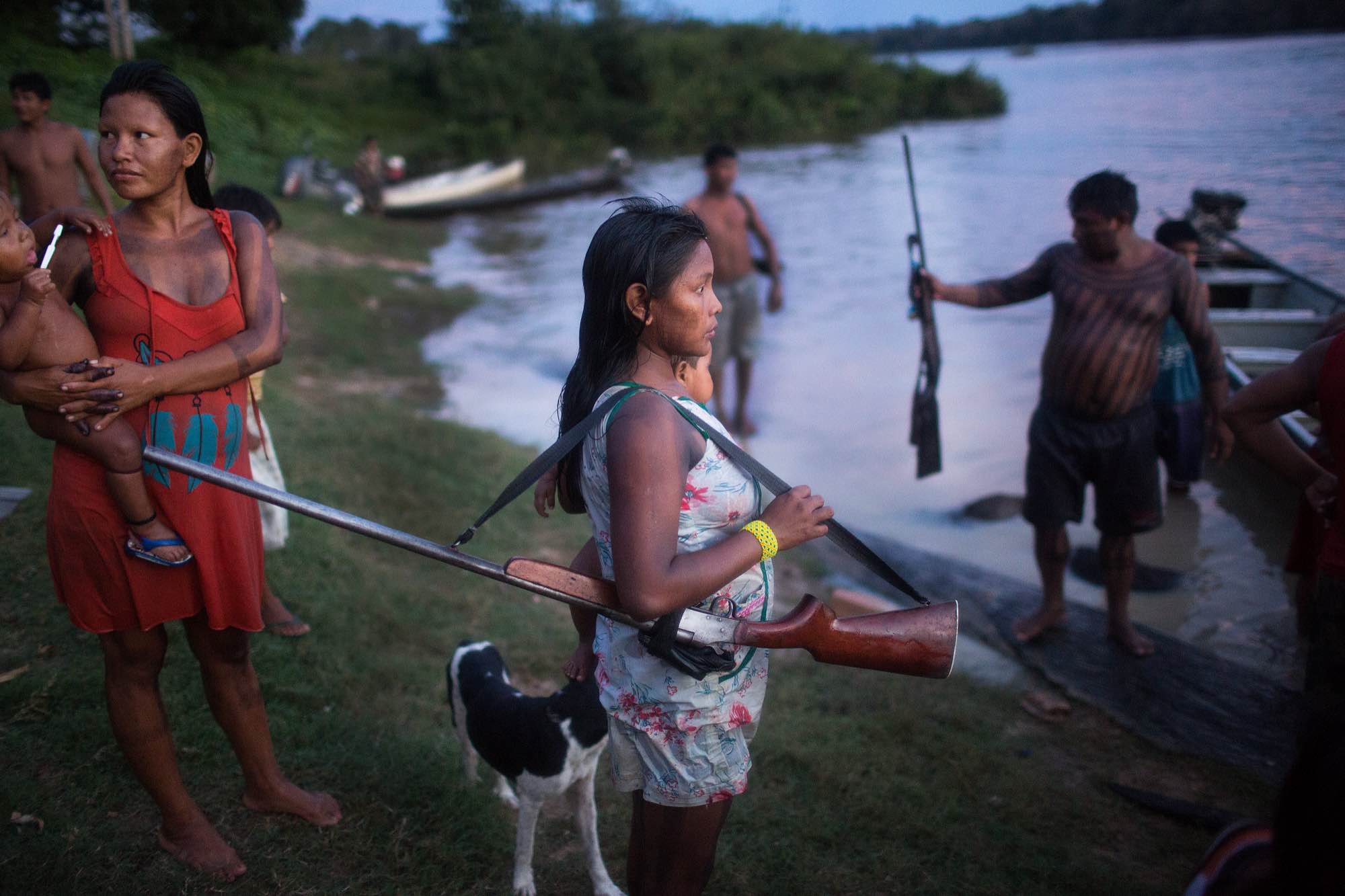 A Xikrin woman holds her husband's shotgun while he cleans freshly hunted peccary in the river.