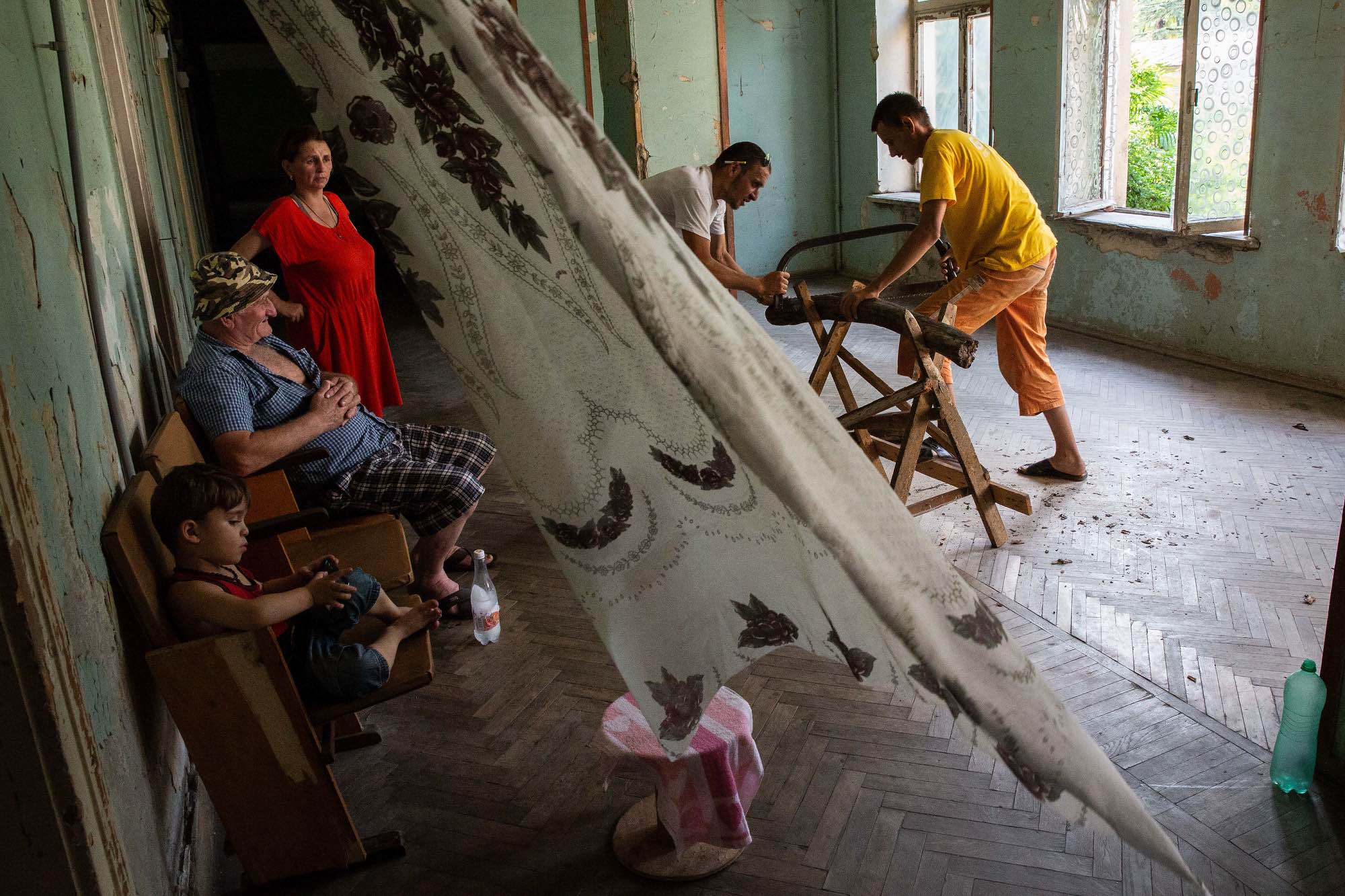 Roman Masivani (yellow shirt) and Tristan Gigusiani (white) cut wood in a hallway at Sanatorium Tskaltubo in Tskatulbo, Georgia on June 15, 2019.