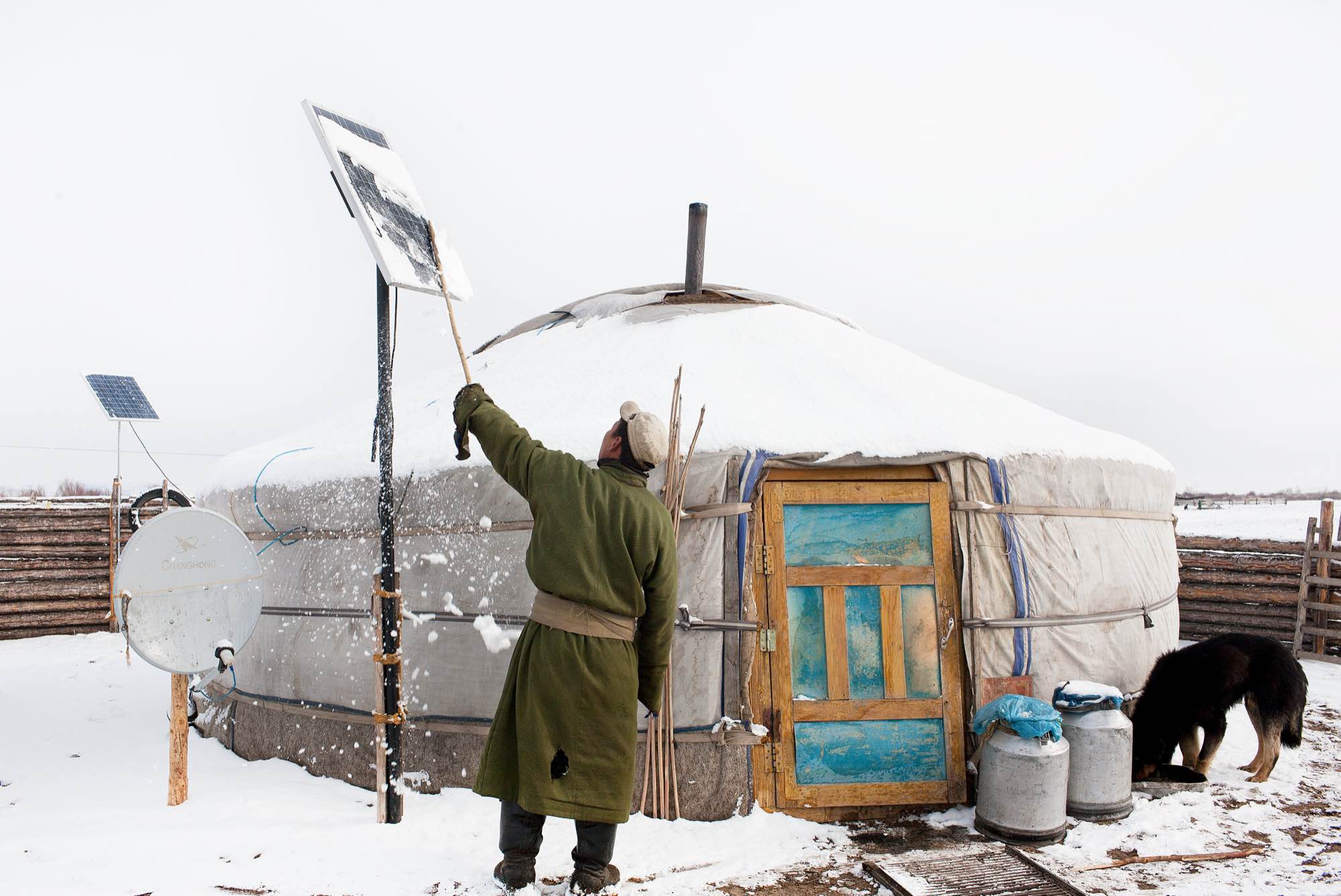 After an overnight snowstorm, a nomad brushes snow off of his solar unit, which powers the lightbulb, TV, and cell phone in his ger (yurt).