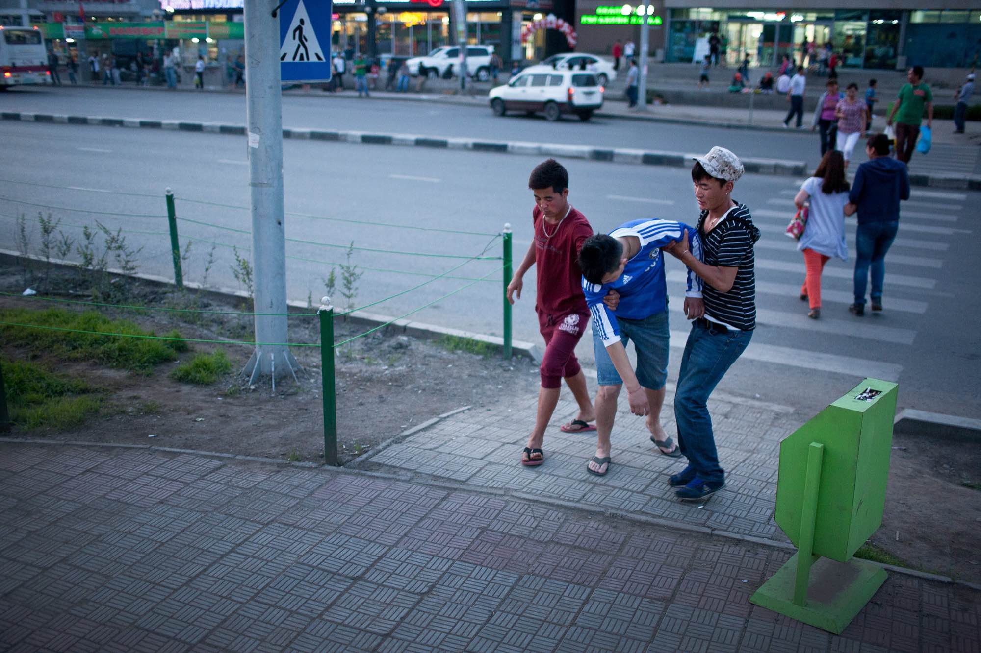 Two young men help their drunk friend to a waiting car.