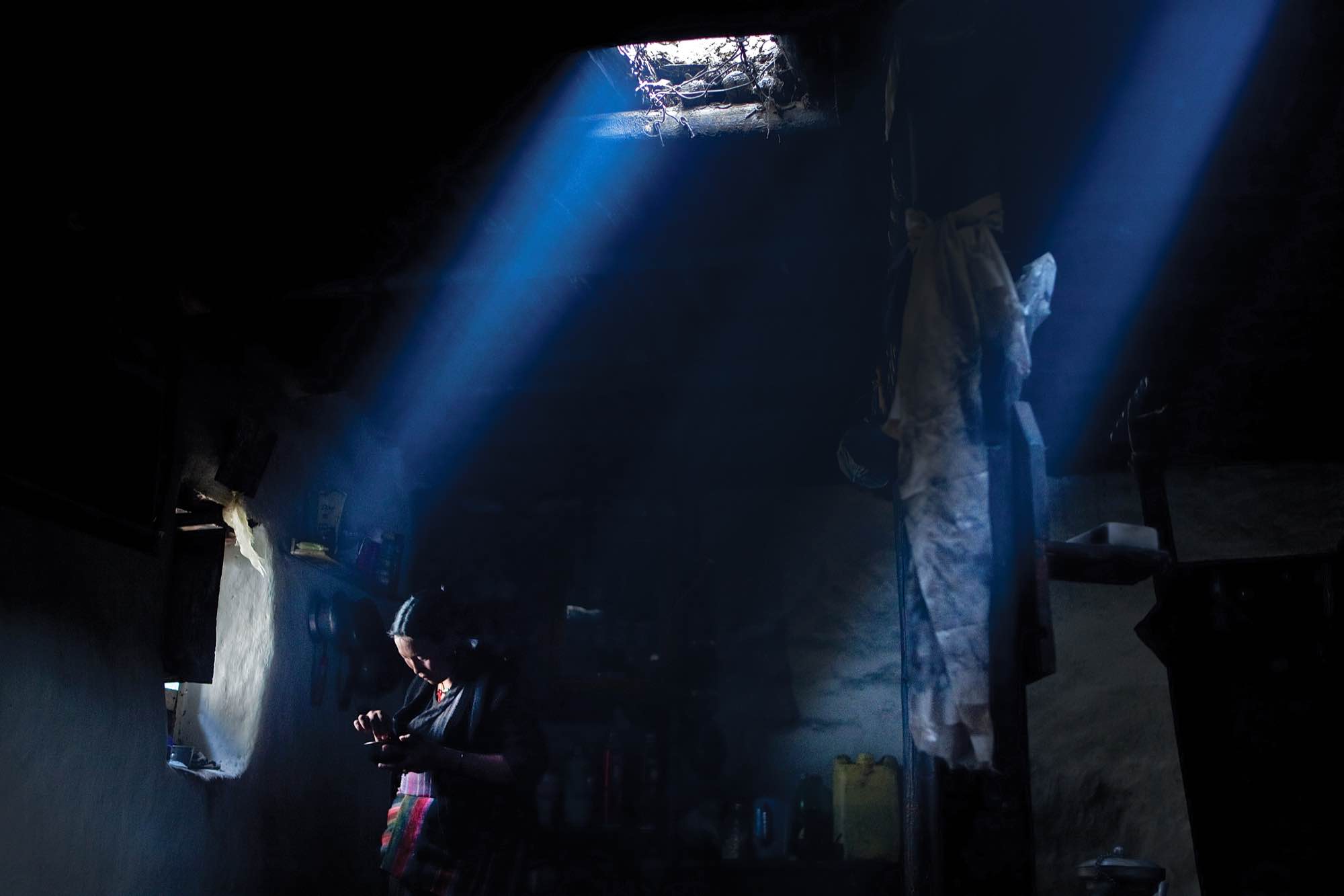 Tashi Dolkar Gurung, a Loba woman, removes gravel from rice near the light of a window in her earthen home in Lo Manthang.